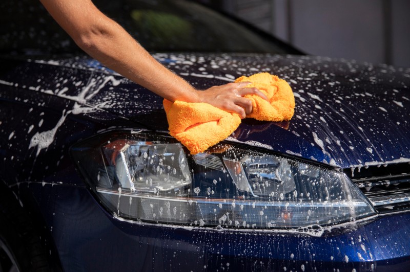 Car bonnet covered in shampoo, a hand holds a lint-free cloth ready to wipe clean