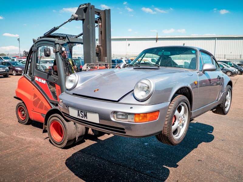Forklift truck lifting and moving a car for recycling