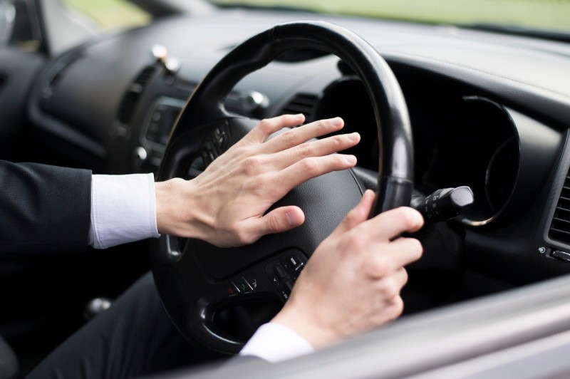 Man pressing palm on a car steering wheel horn
