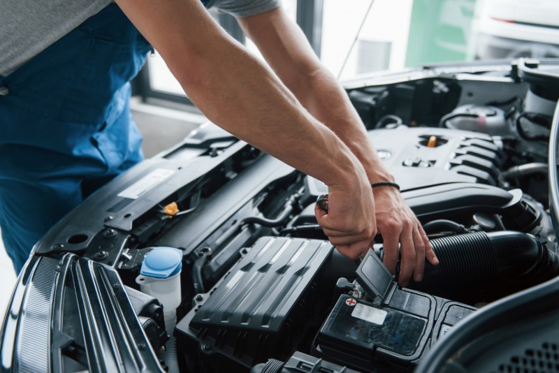 Man working with car battery positive terminal under the hood