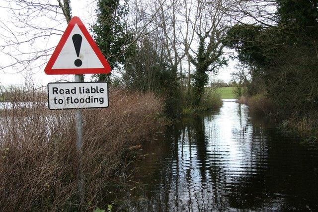 Sign says 'Road liable to flooding' adjacent a flooded road