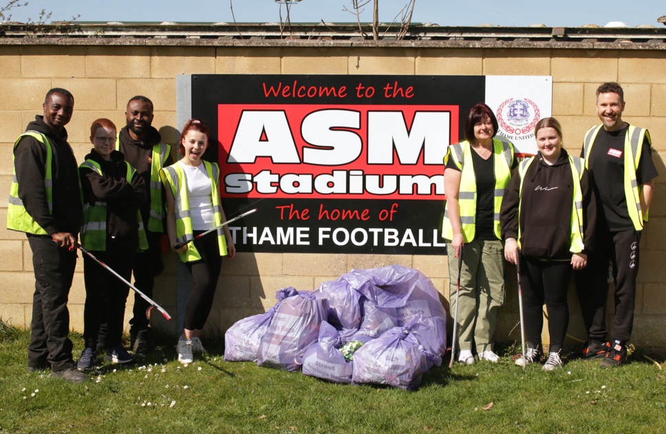ASM Auto Recycling staff beside the Thame FC ASM Stadium sign with full waste sacks